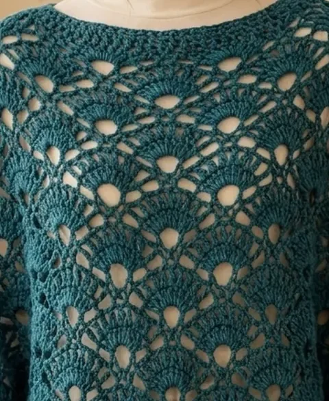 A deep teal crochet poncho worked in an open peacock fan lace stitch